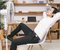 Young Asian office worker resting on chair in front of ventilator and refreshing from heat at office