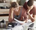 Worried couple reviewing their family finances and calculating expenses, trying to save some money to pay off loan in bank, reviewing bills together, using laptop and calculator at kitchen table