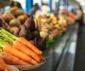 Close-up focused view over organic raw carrots and beetroots sorted in different plates on the counter. Blurred vegetables in the background. Local market.