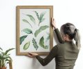 Young woman hanging a frame of leaf print painting on the wall